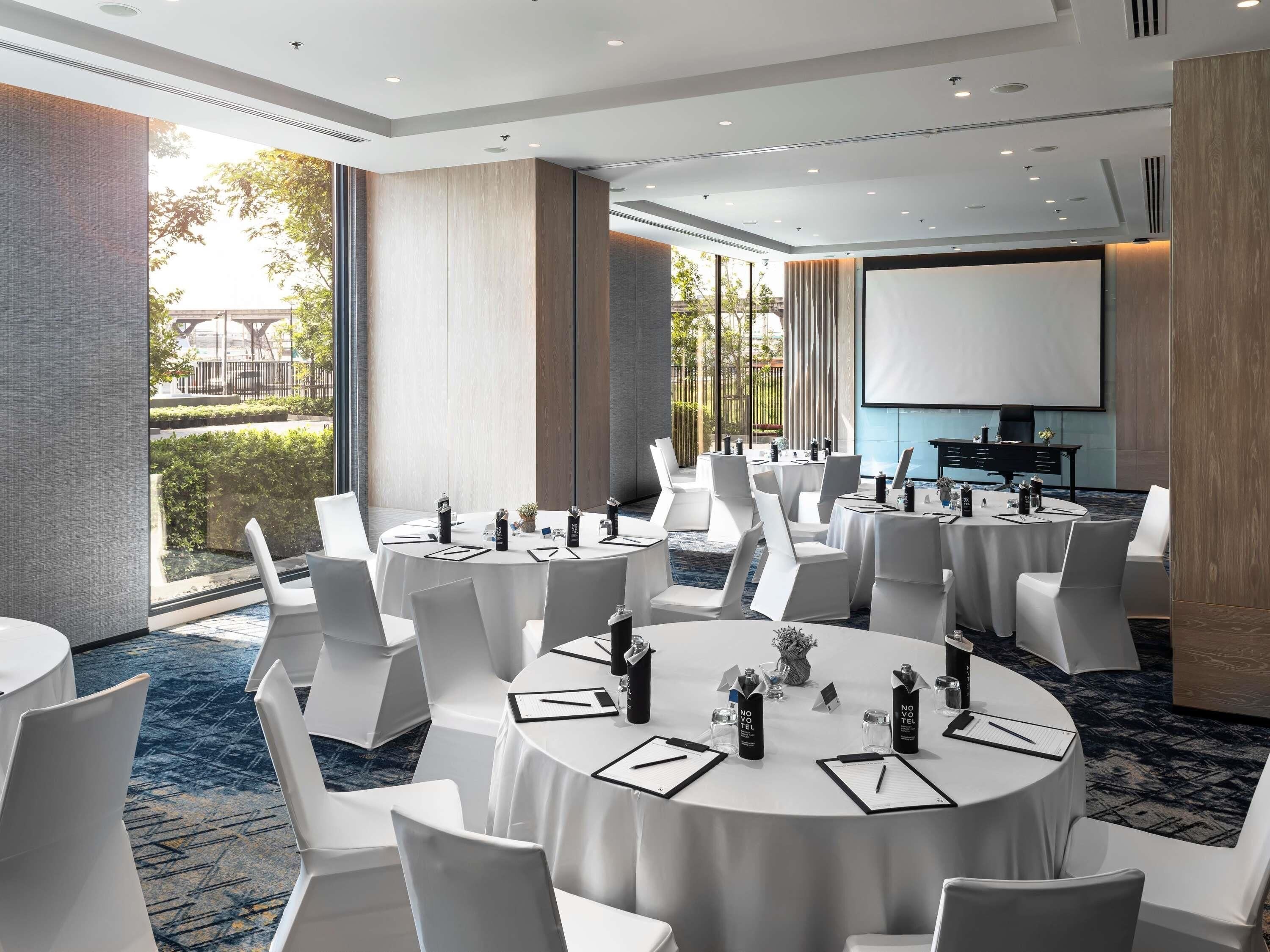 A conference room with round tables, white chairs, and a projector screen.