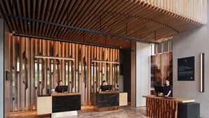 A reception area with wooden slats and marble flooring, featuring two reception desks and a sign on the wall. - Novotel Bangkok Future Park Rangsit (Thanyaburi)