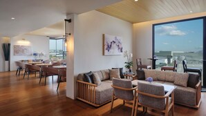 A spacious living area with a large window, a sofa set, a dining table, and a view of the cityscape. - Novotel Bangkok Future Park Rangsit (Thanyaburi)
