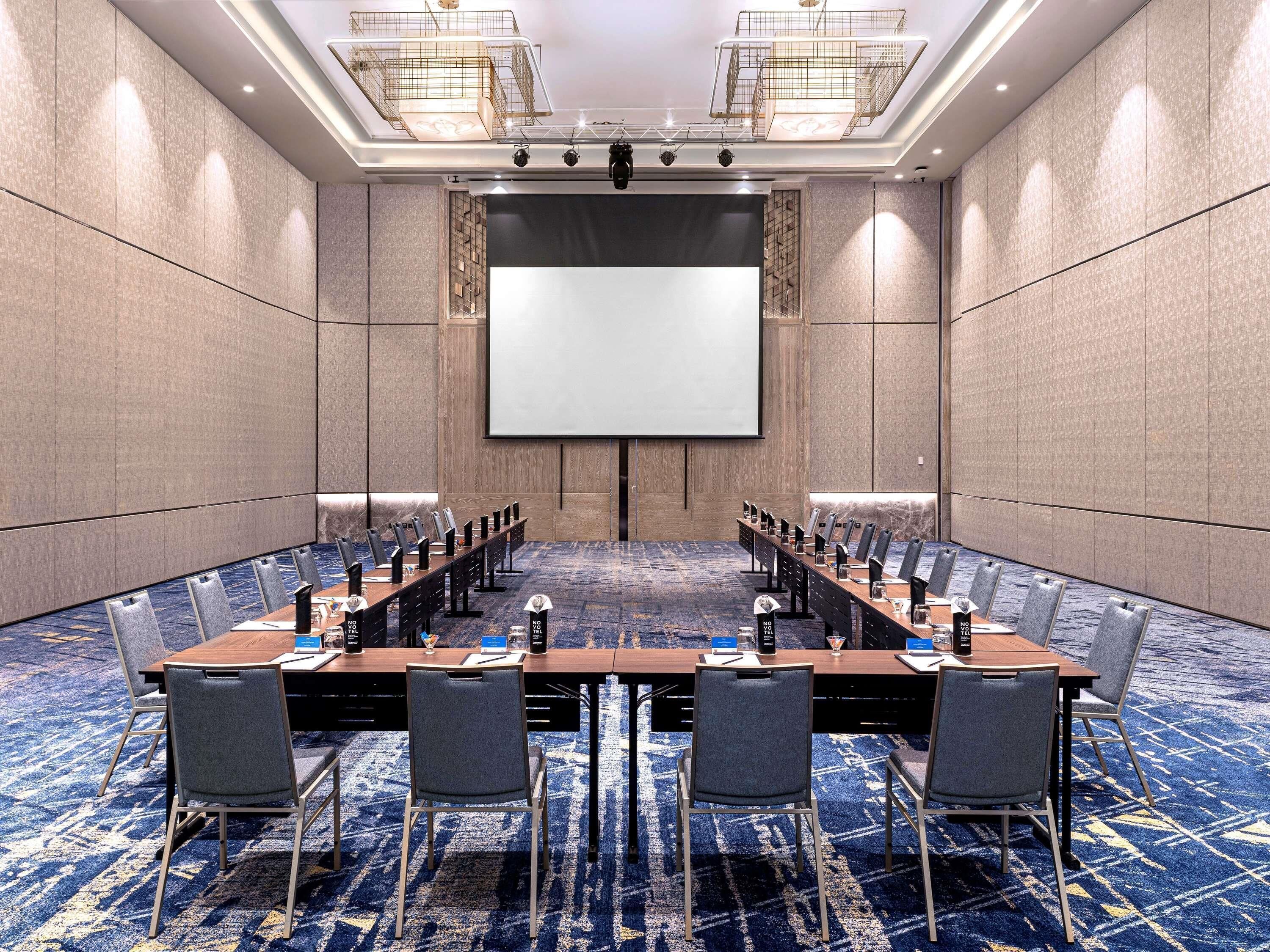 A conference room with a long table, chairs, a projector screen, and a carpeted floor.