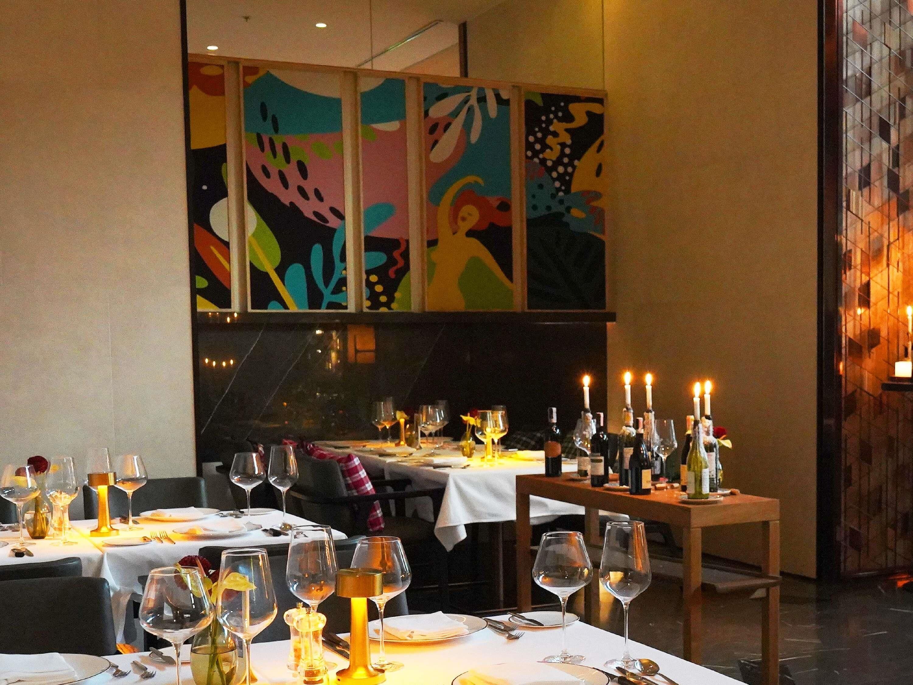 A restaurant with tables set for dining, wine glasses, and candles.