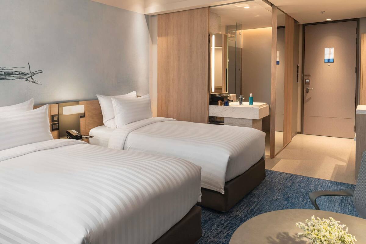 A hotel room with two beds, a bathroom with a mirror, and a small table with flowers.