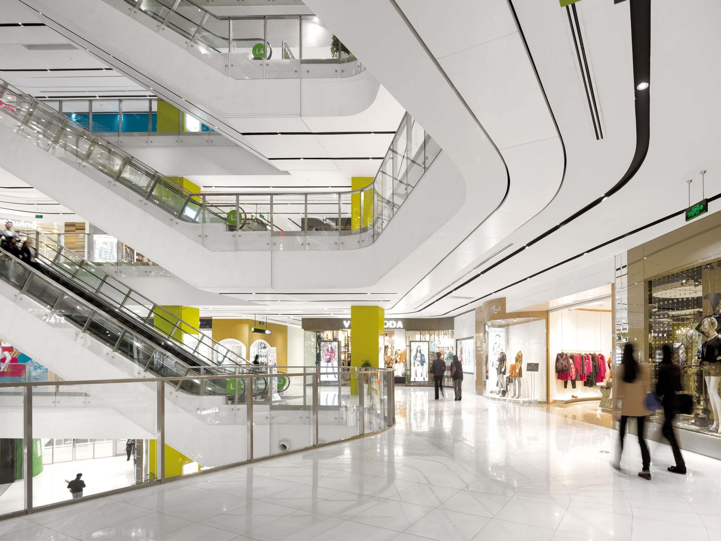 A multi-level shopping mall with escalators, glass railings, and various retail stores.