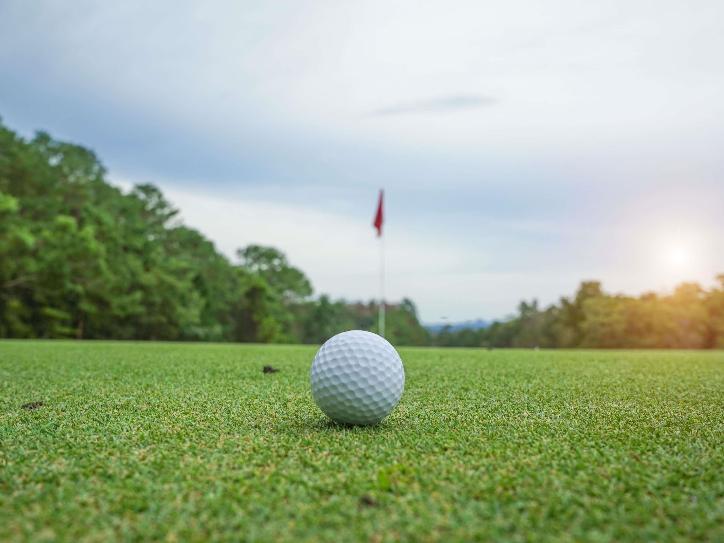Una pelota de golf sobre un campo verde, con una bandera al fondo.