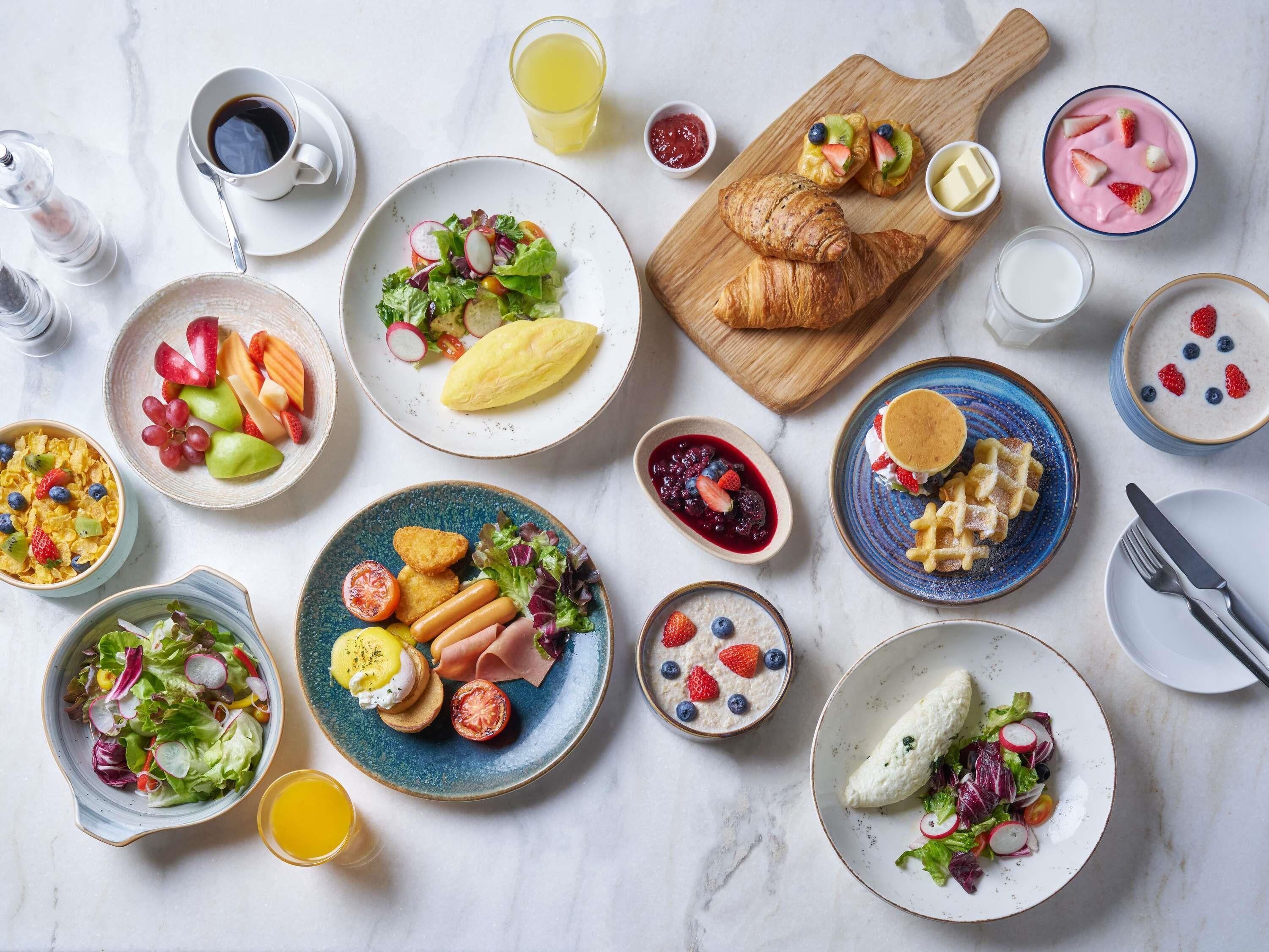 A variety of breakfast dishes including croissants, fruit, yogurt, and waffles.