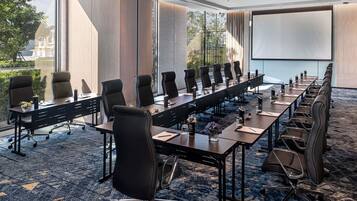 Una sala de conferencias con mesas largas, sillas y una pantalla para proyector.