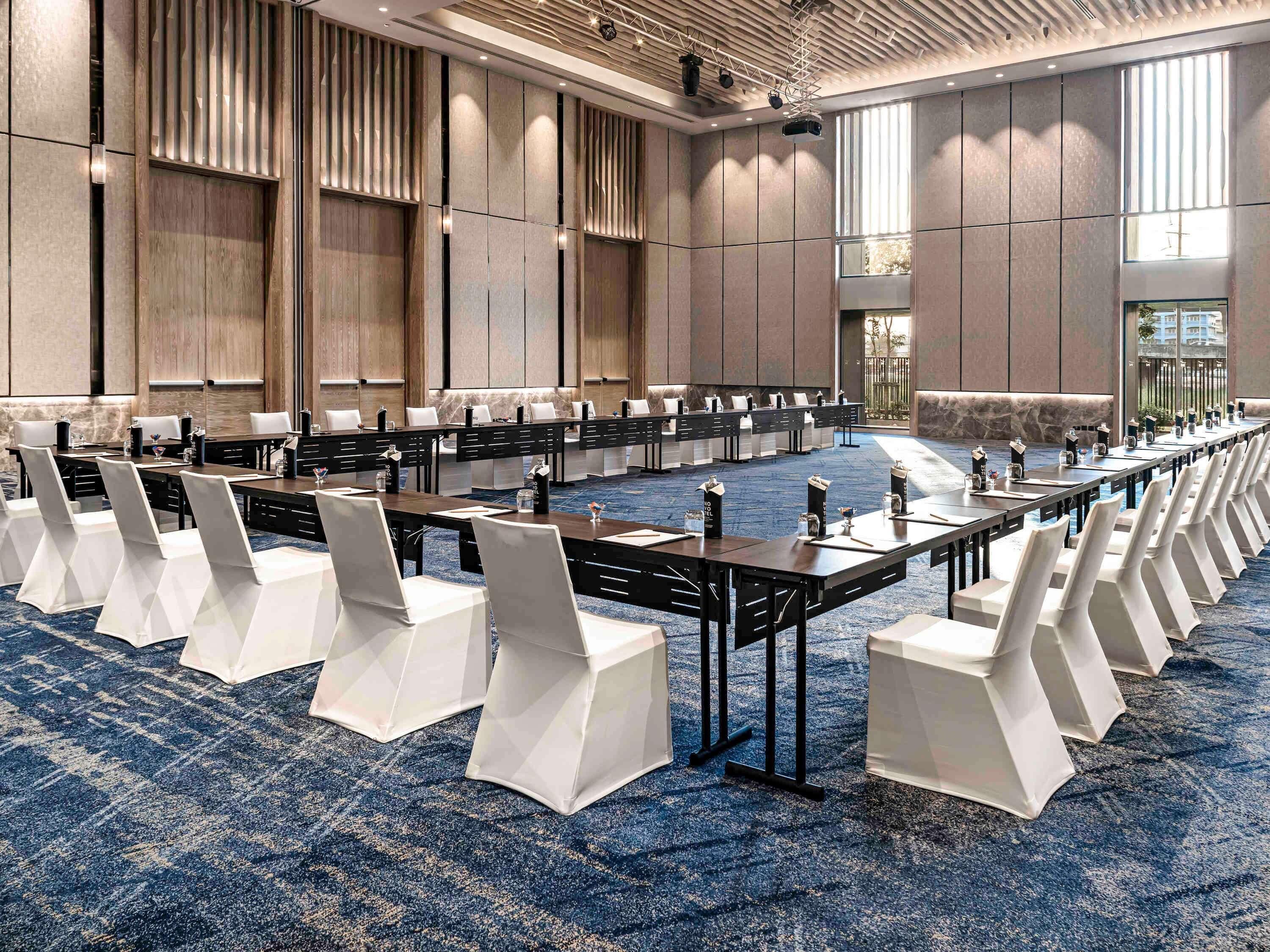 A conference room with long tables, white chairs, and a blue carpet.