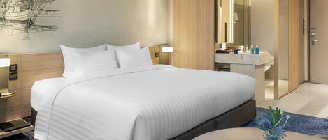 Una habitación de hotel moderna con una cama grande, mesitas de noche, una mesita auxiliar redonda y un baño con espejo y lavamanos.