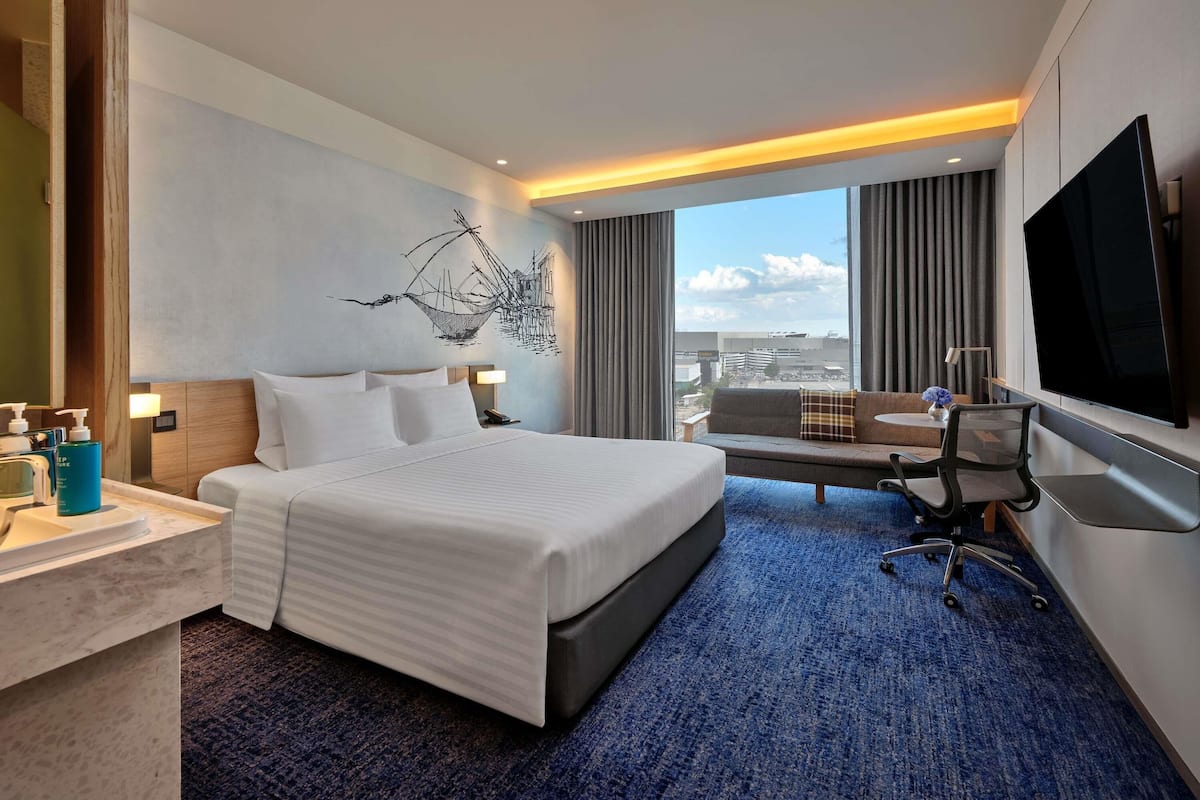 Une chambre dâhĂŽtel Ă©quipĂ©e dâun lit, dâun bureau, dâune chaise, dâune tĂ©lĂ©vision et dâune grande fenĂȘtre donnant sur la ville.