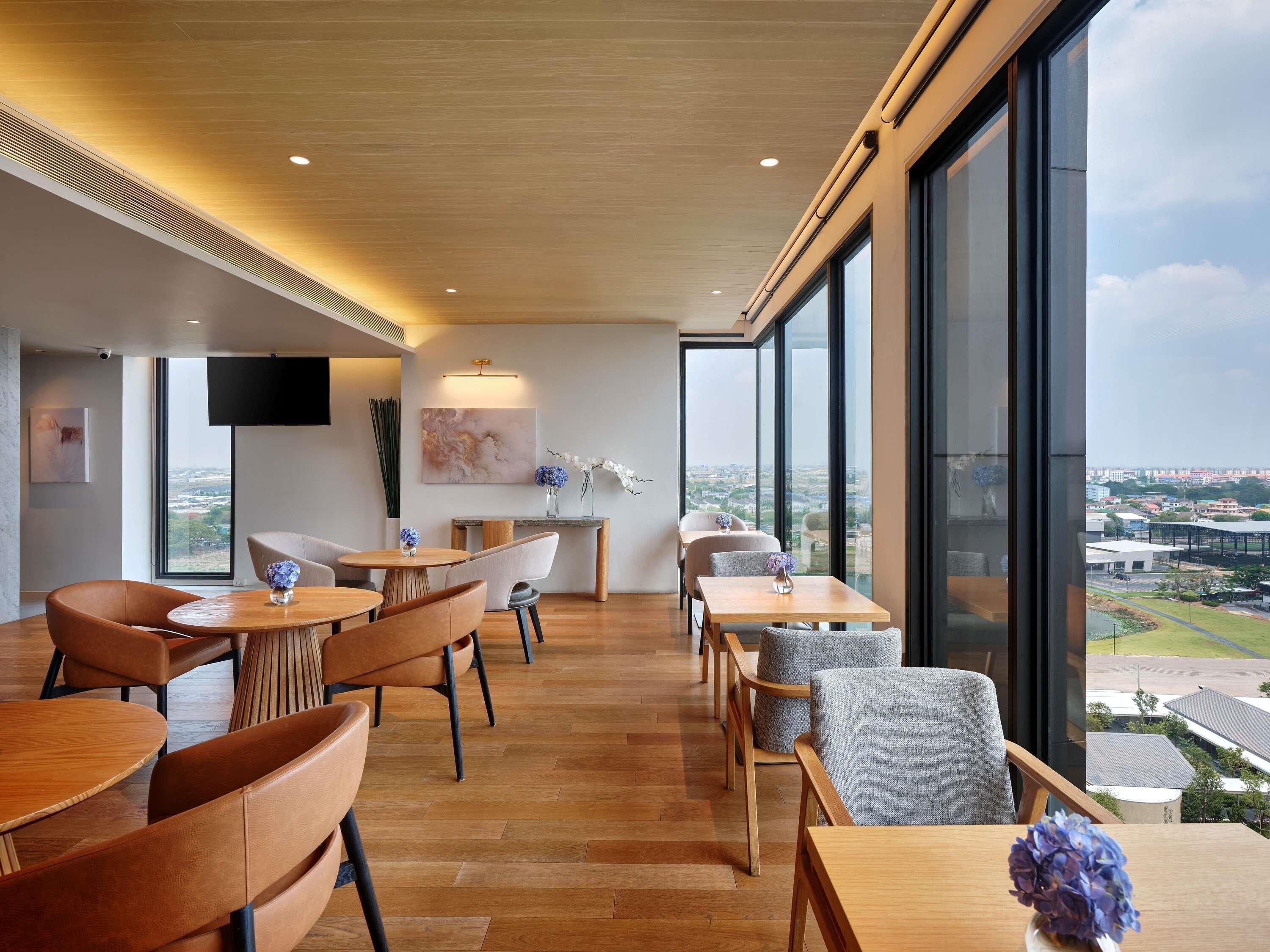 Un interior moderno con suelo de madera, un comedor con mesas y sillas, un ventanal con vistas a la ciudad y un televisor de pantalla plana montado en la pared.