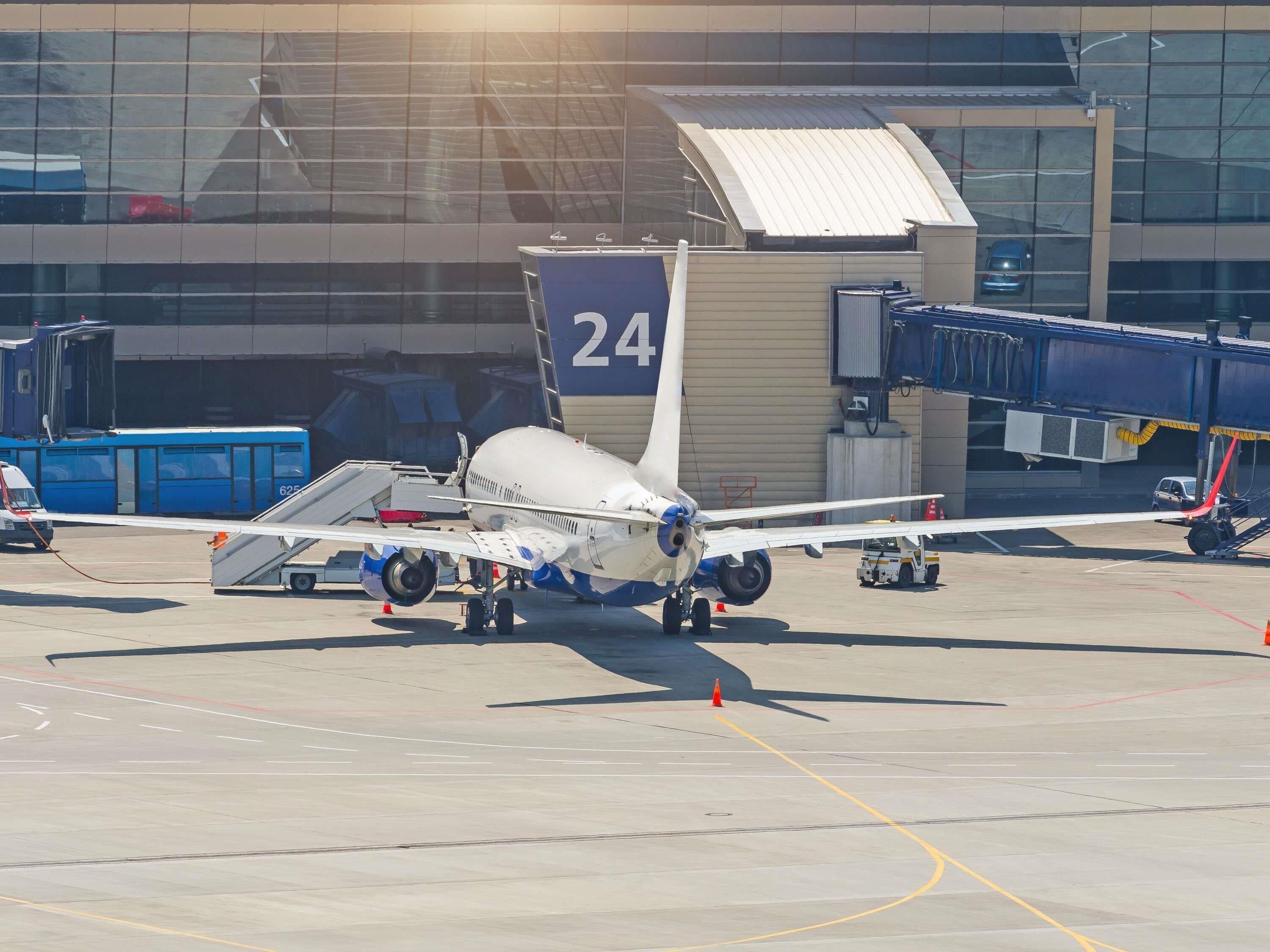 An airport terminal with a parked airplane, a jet bridge, and a baggage carousel.