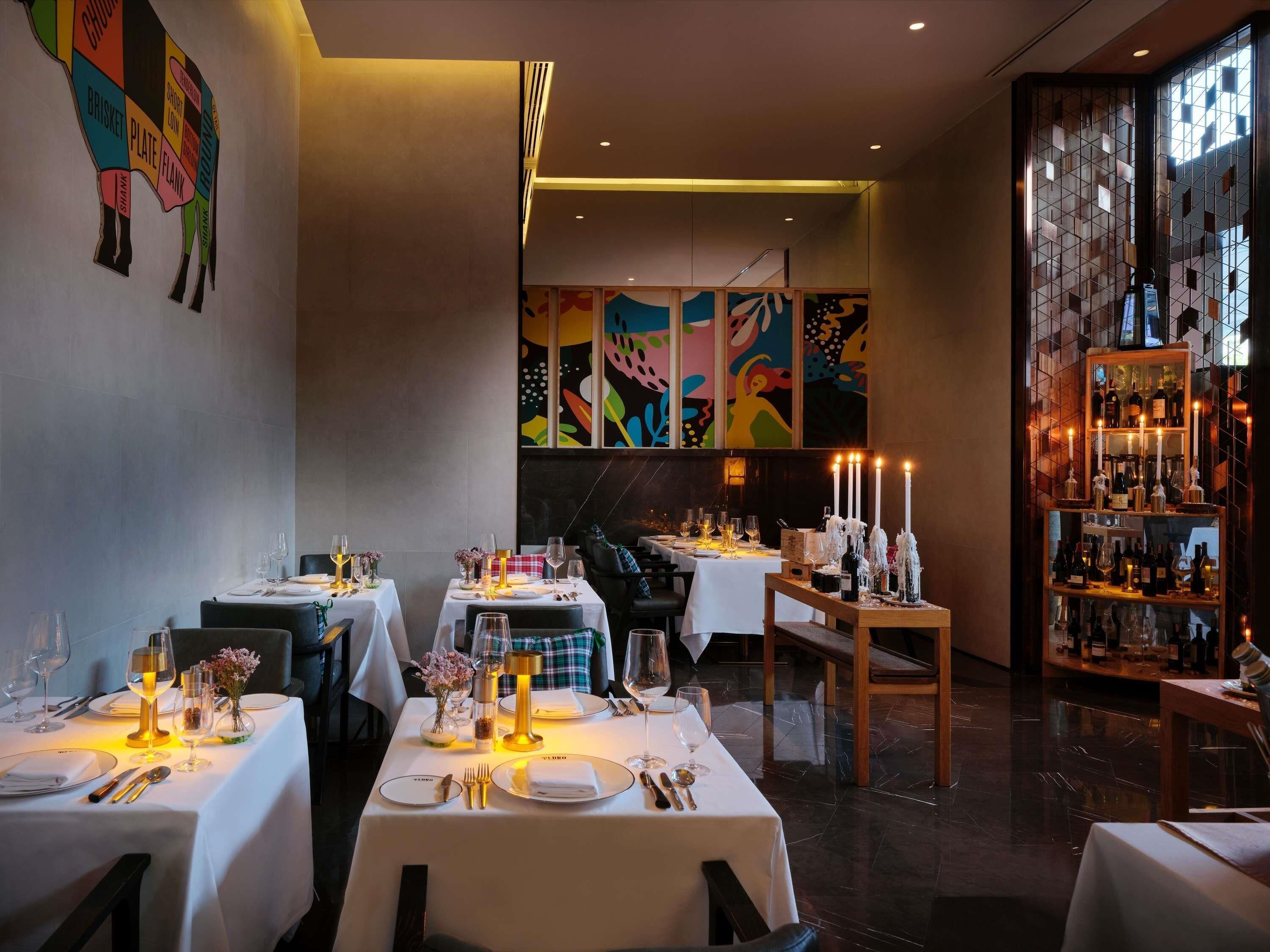 A restaurant interior with tables set for dining, a bar area with bottles, and a colorful abstract painting on the wall.