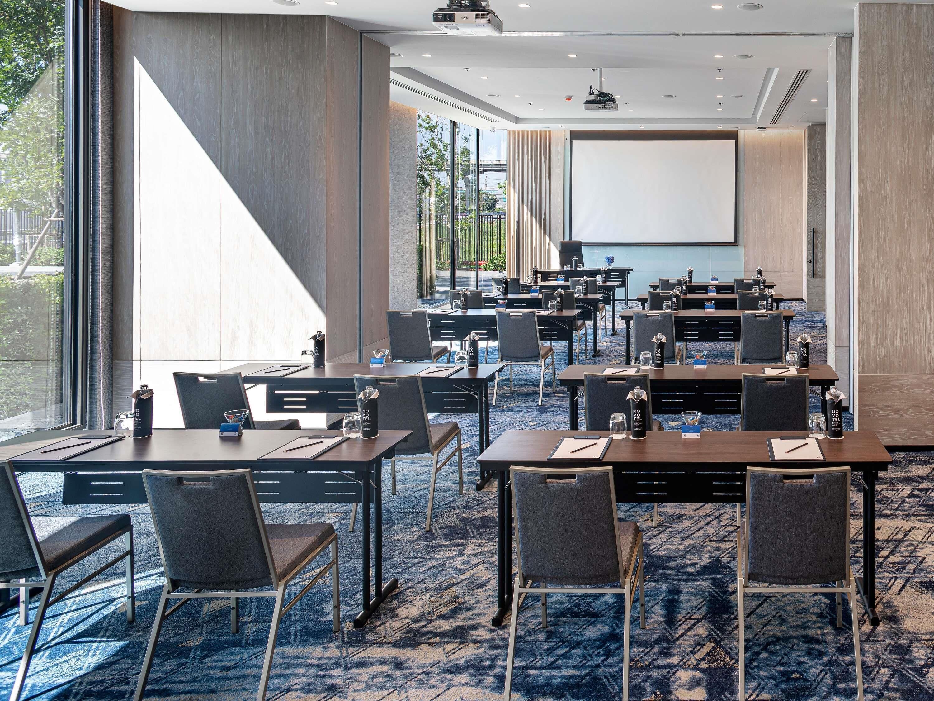 A conference room with tables, chairs, a projector screen, and a large window.