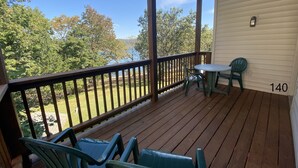A wooden deck with a table and chairs, overlooking a lake and trees.