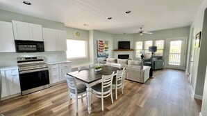 A spacious kitchen with white cabinets, a microwave, and a stove. There is a dining area with a wooden table and white chairs.