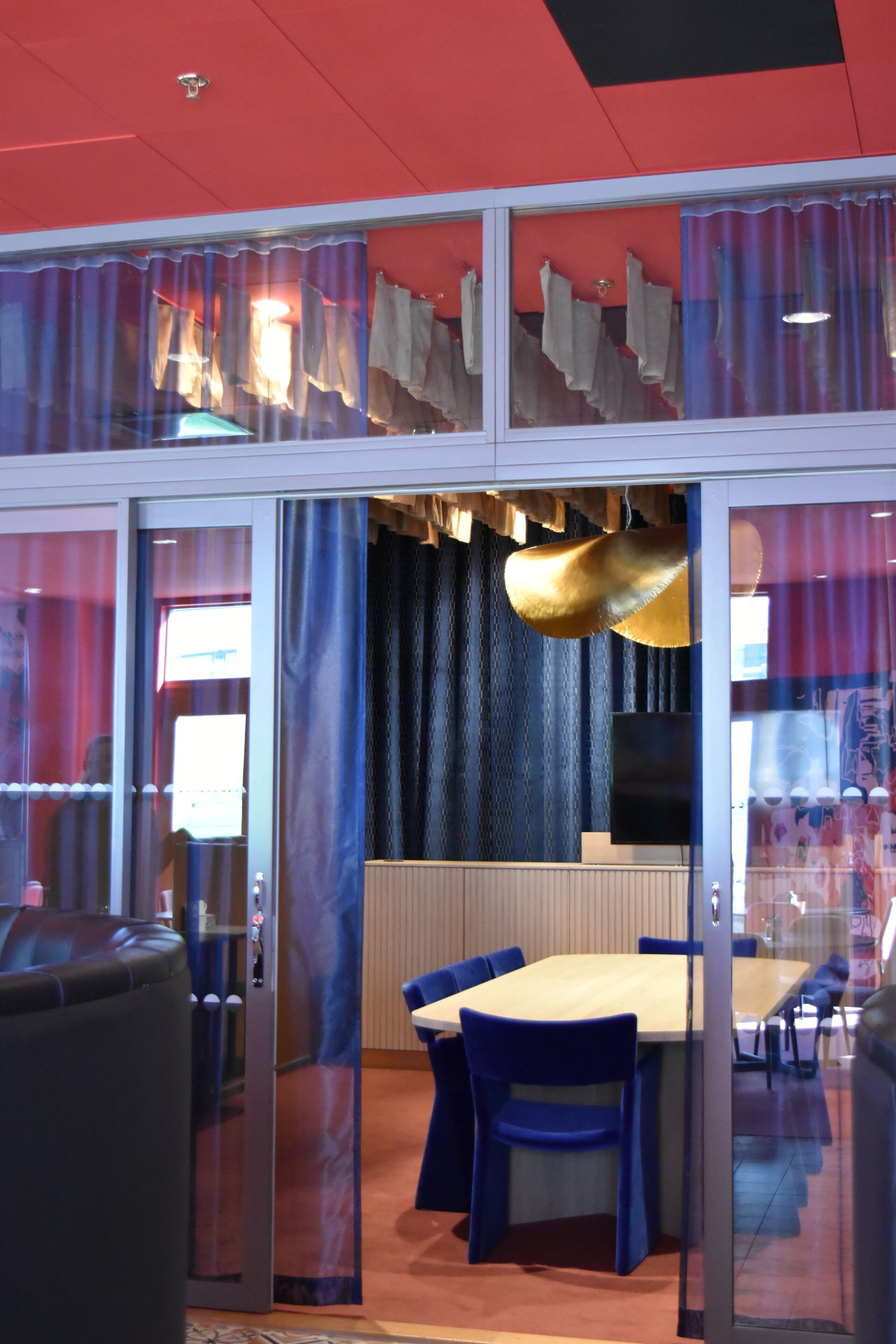 A modern interior with a glass partition, a wooden table, blue chairs, and a hanging light fixture.