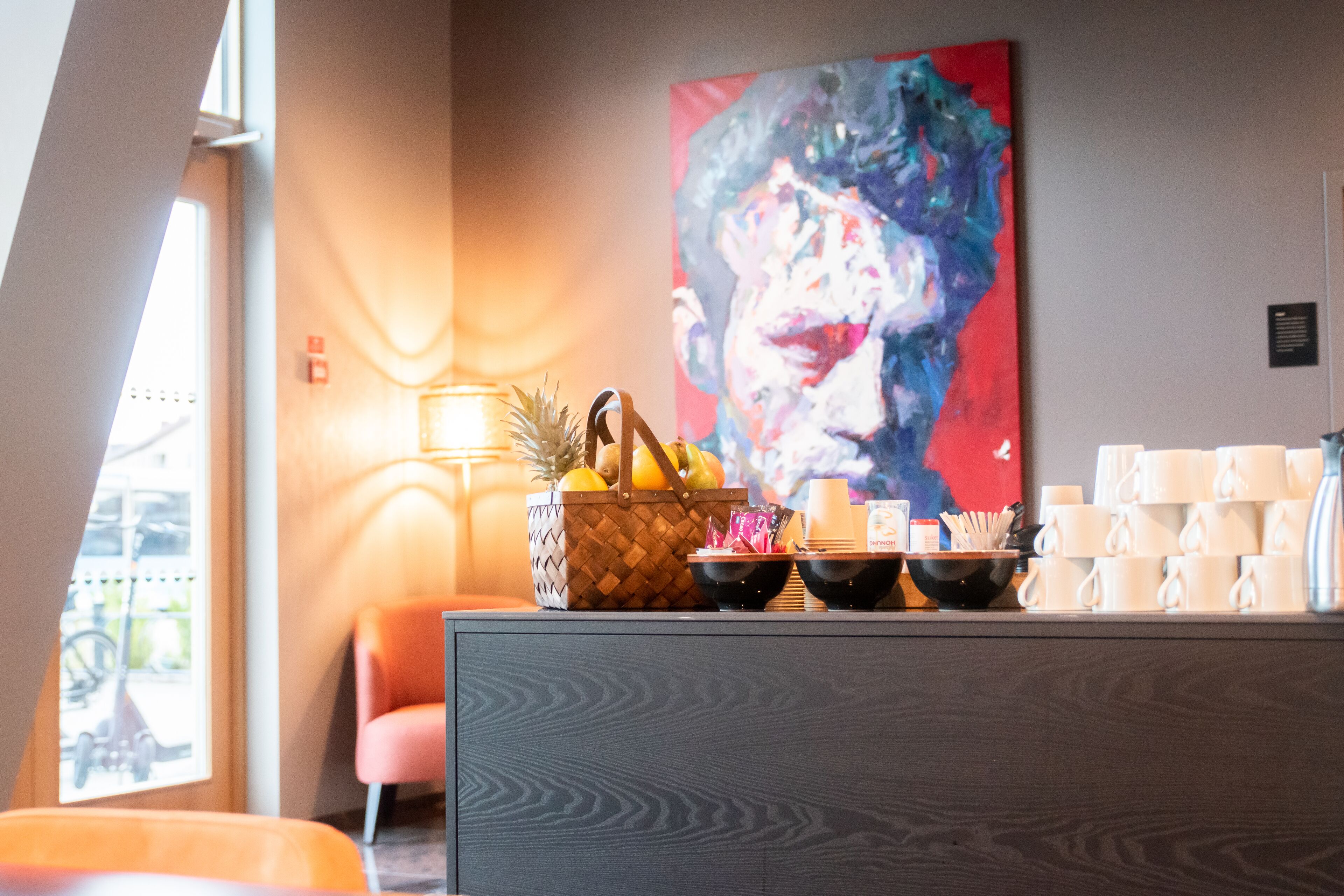 A modern interior with a wooden cabinet, a fruit basket, and a large abstract painting on the wall.