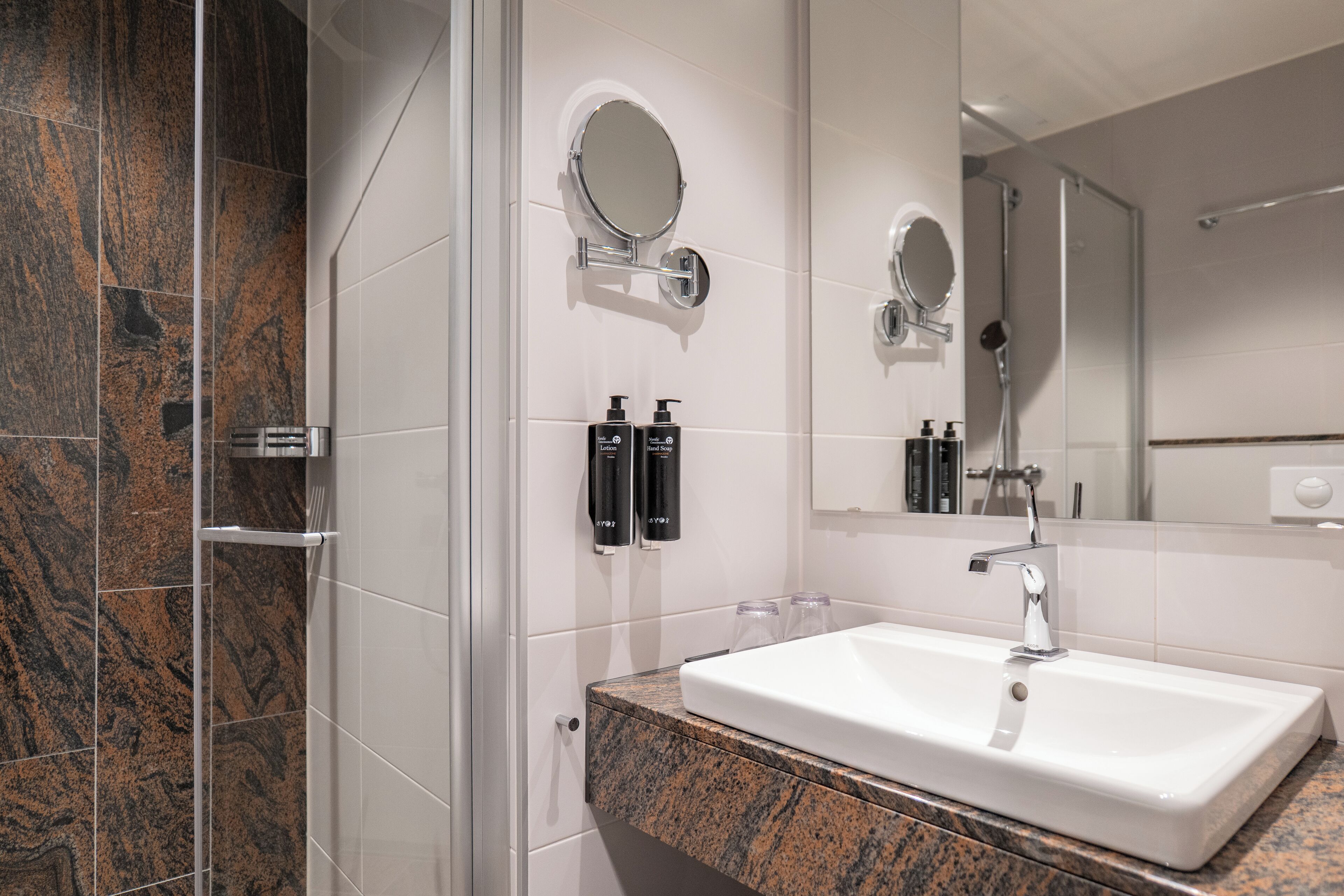 Un baño moderno con un lavamanos blanco, encimera de granito y dos espejos redondos sobre el lavamanos.