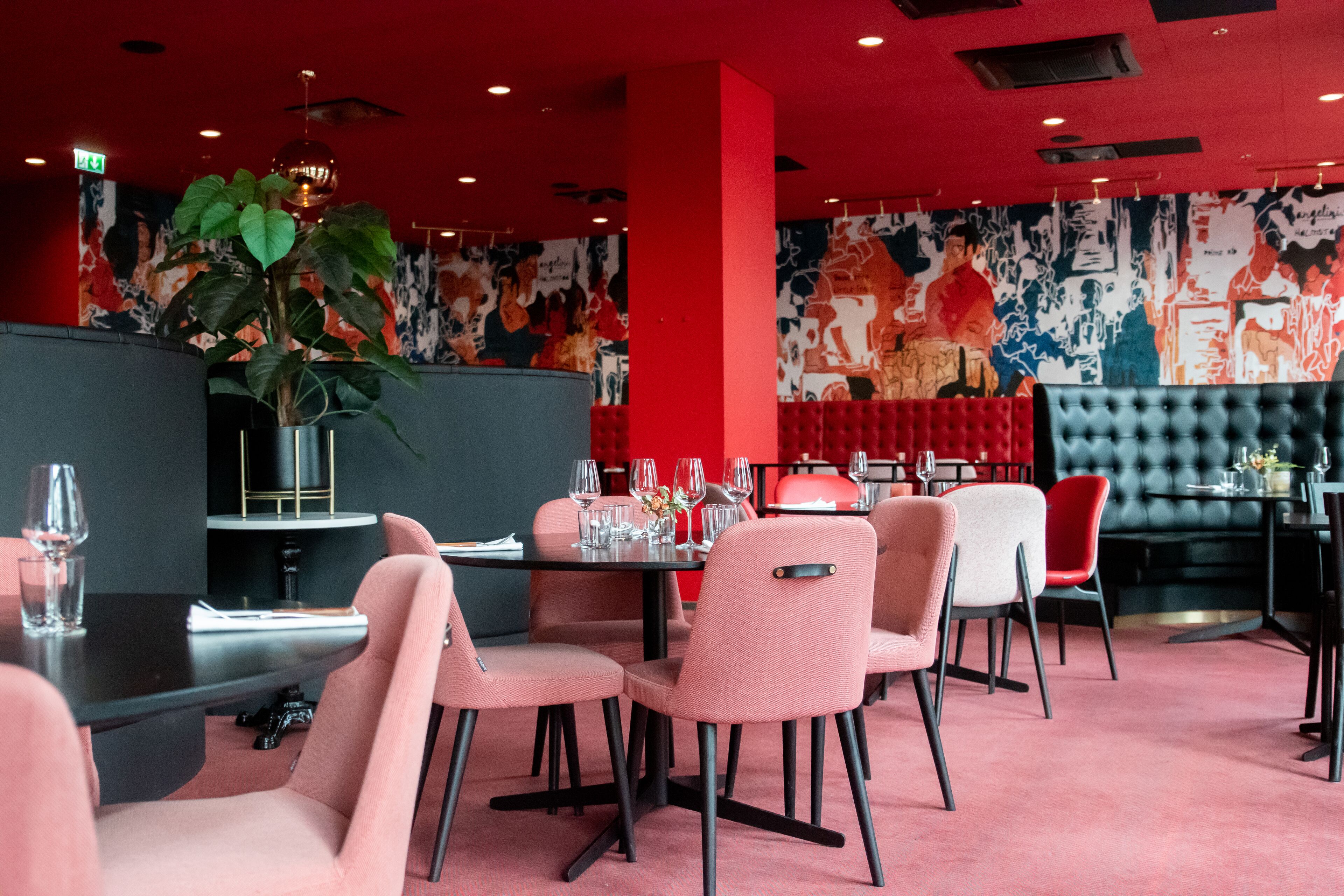 A restaurant interior with red walls, a large mural, and a mix of pink and red chairs.
