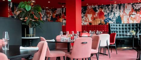 A restaurant interior with red walls, a large mural, and a mix of pink and red chairs.