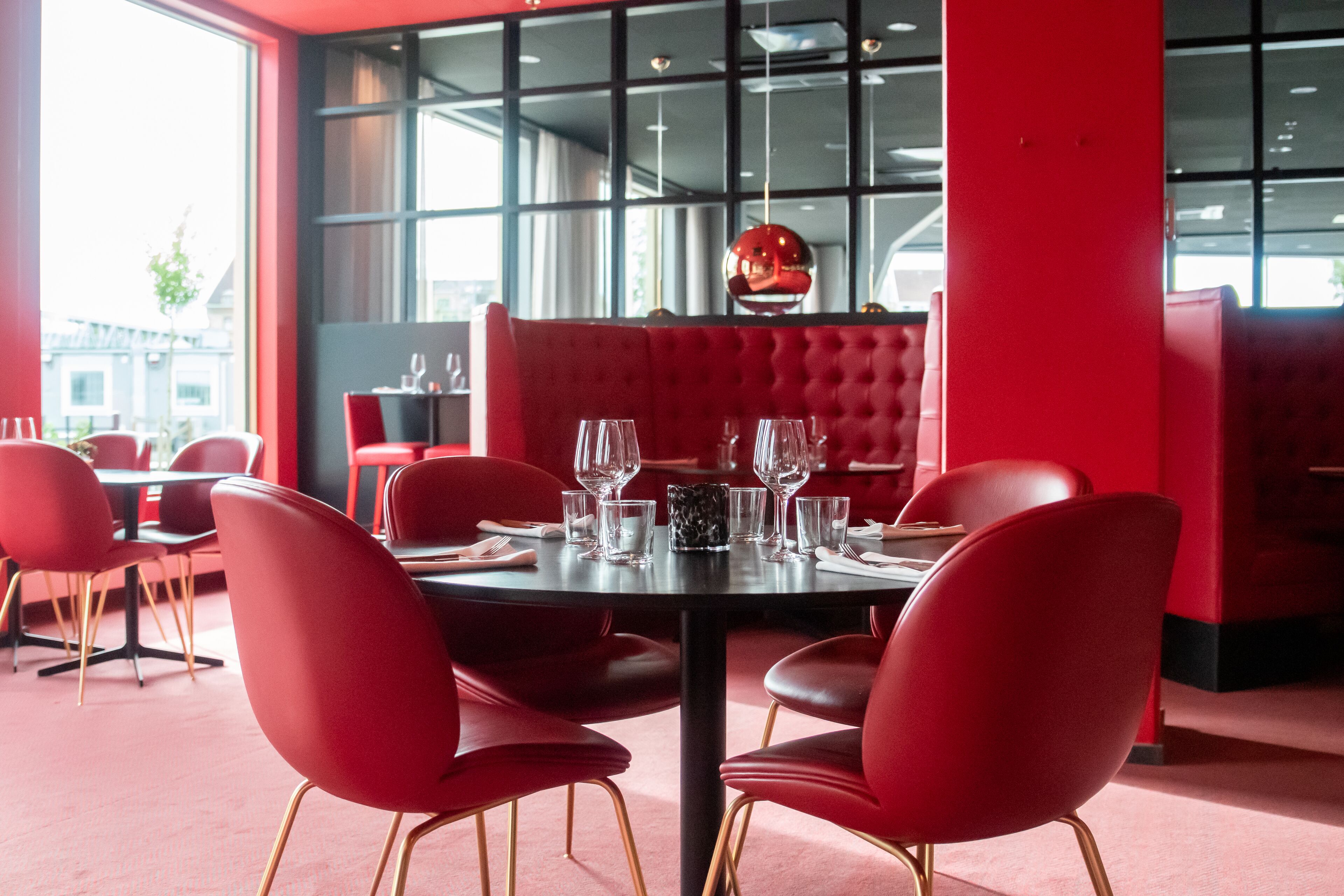 Een eetgedeelte met rode bekleden banken en stoelen, een ronde tafel gedekt voor een maaltijd, en grote ramen met uitzicht op de stad.
