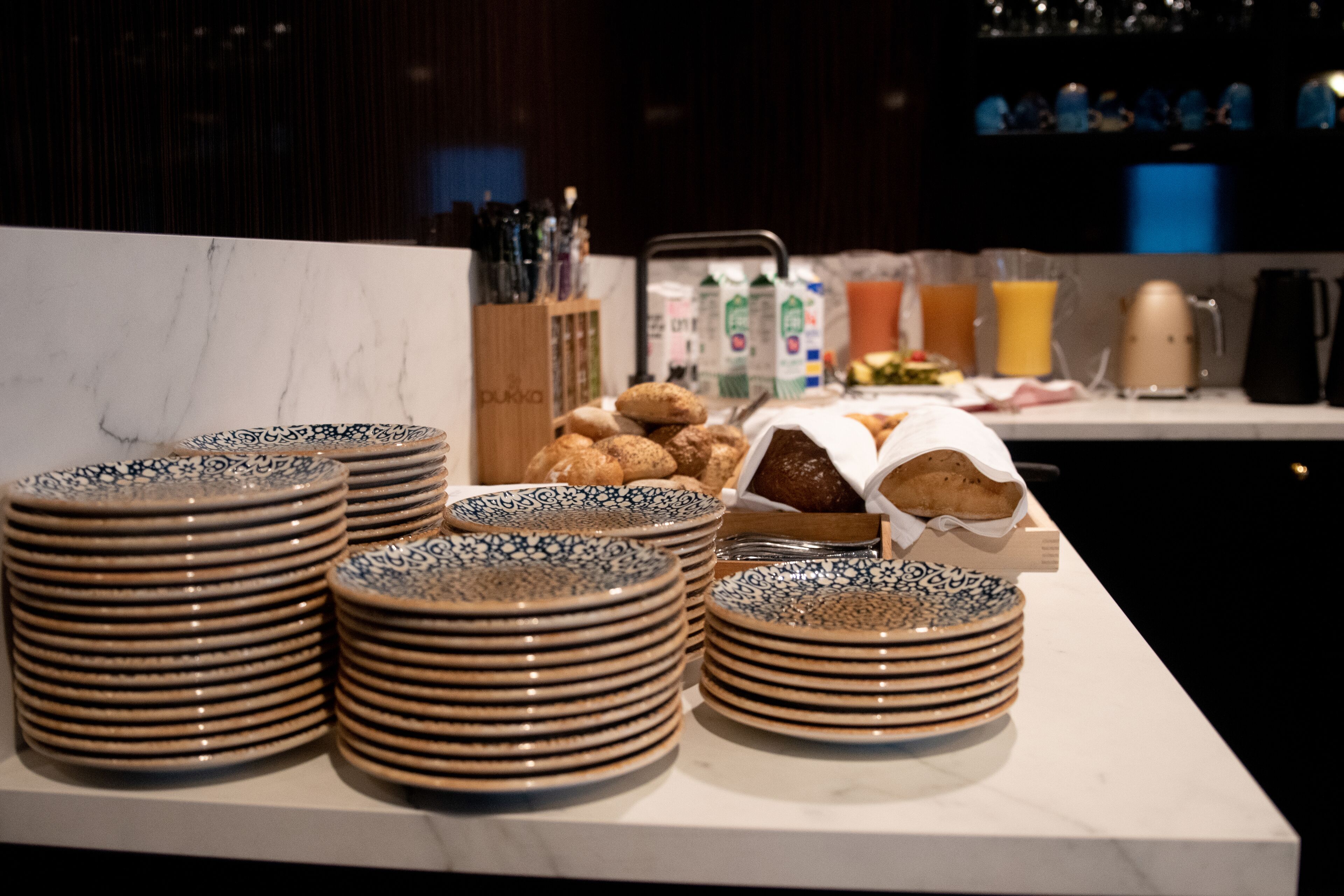 Stacks of patterned plates and a tray of pastries on a marble countertop in a kitchen setting.