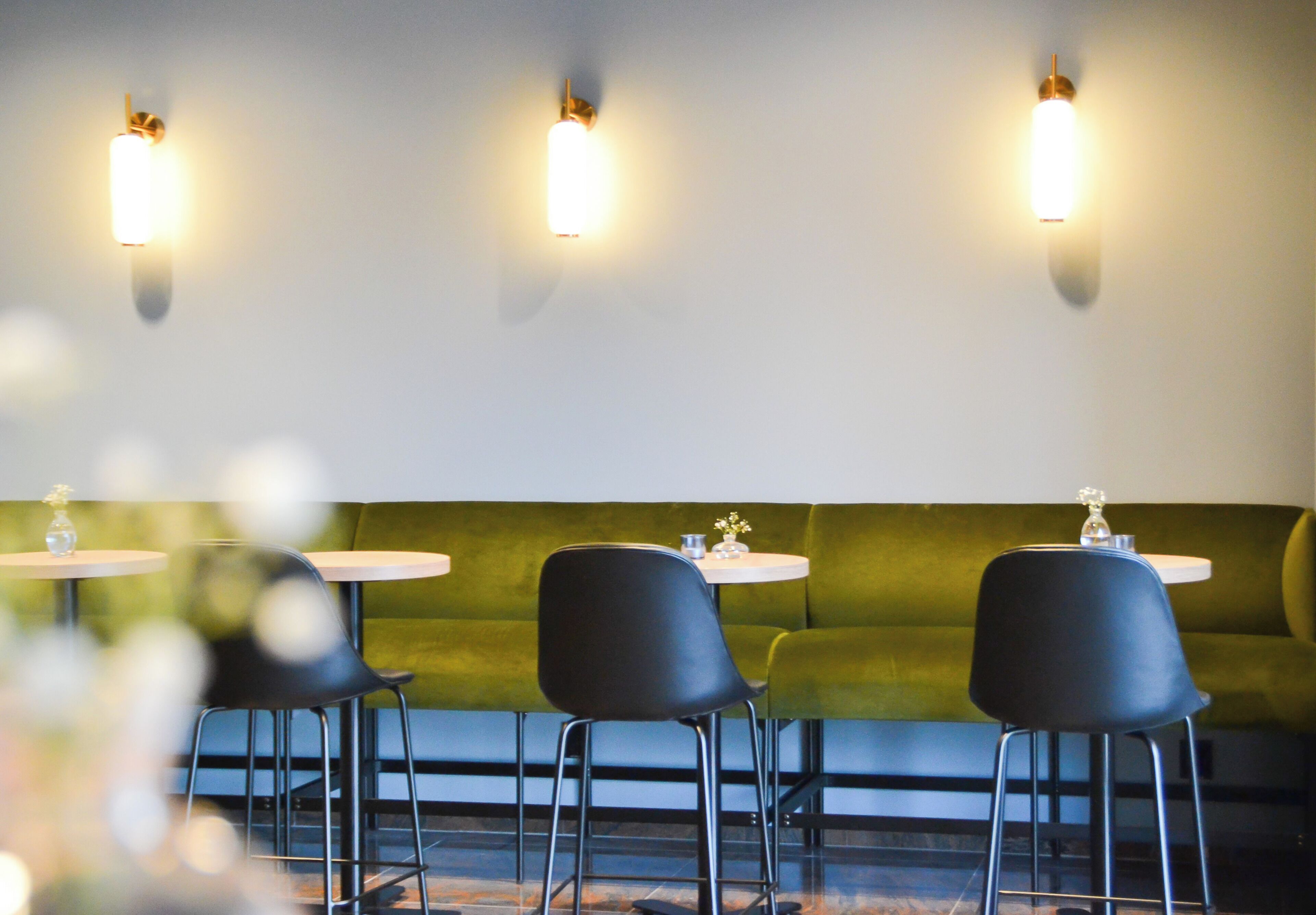 A restaurant interior with a green cushioned bench, black chairs, and round tables.