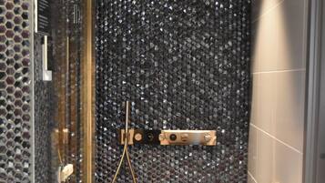 Une douche moderne dotée d’une porte en verre, d’un pommeau de douche à main et d’un panneau de commande fixé au mur.