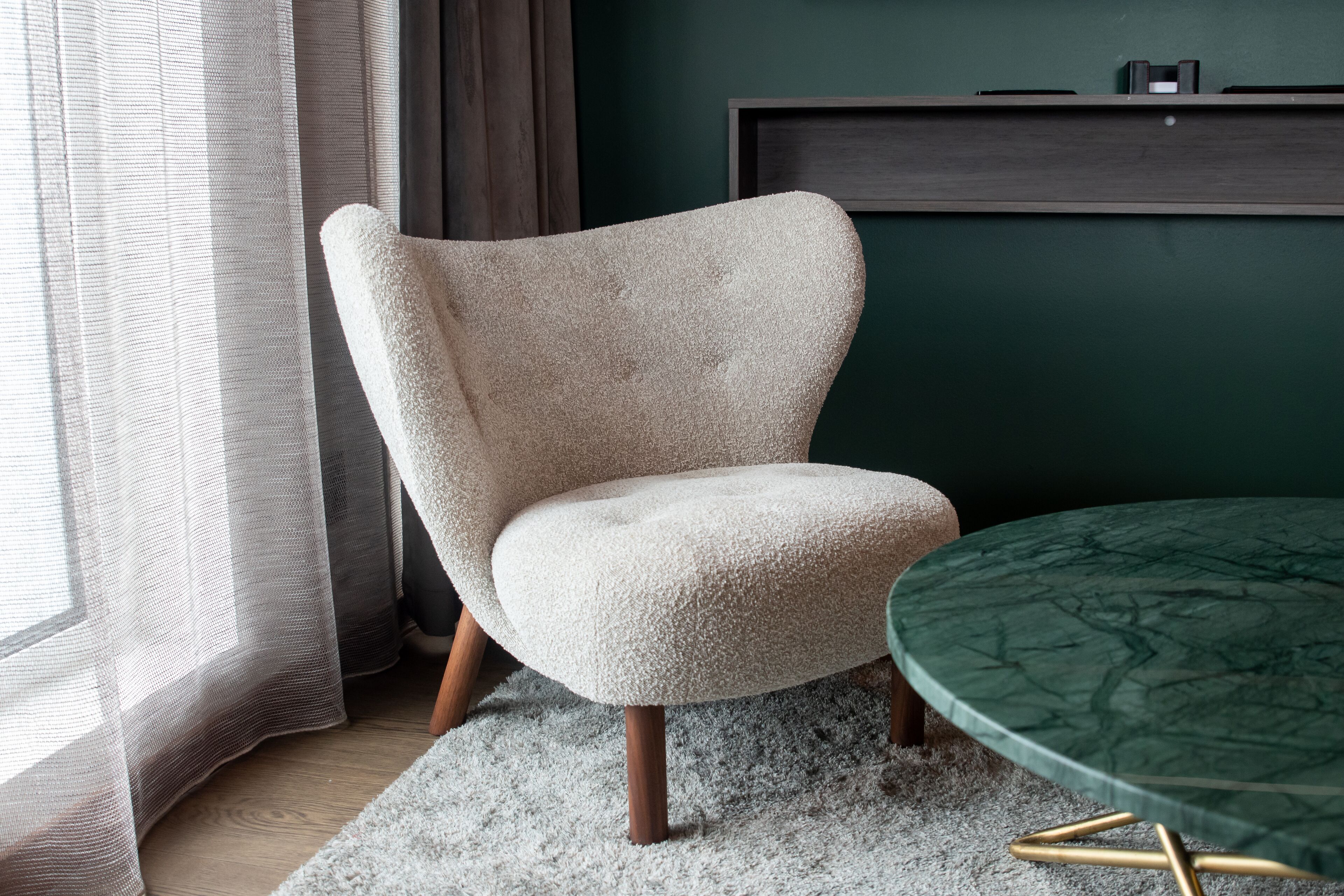 Una habitación moderna con un sillón color crema, una mesa de mármol verde y un estante de madera oscura.