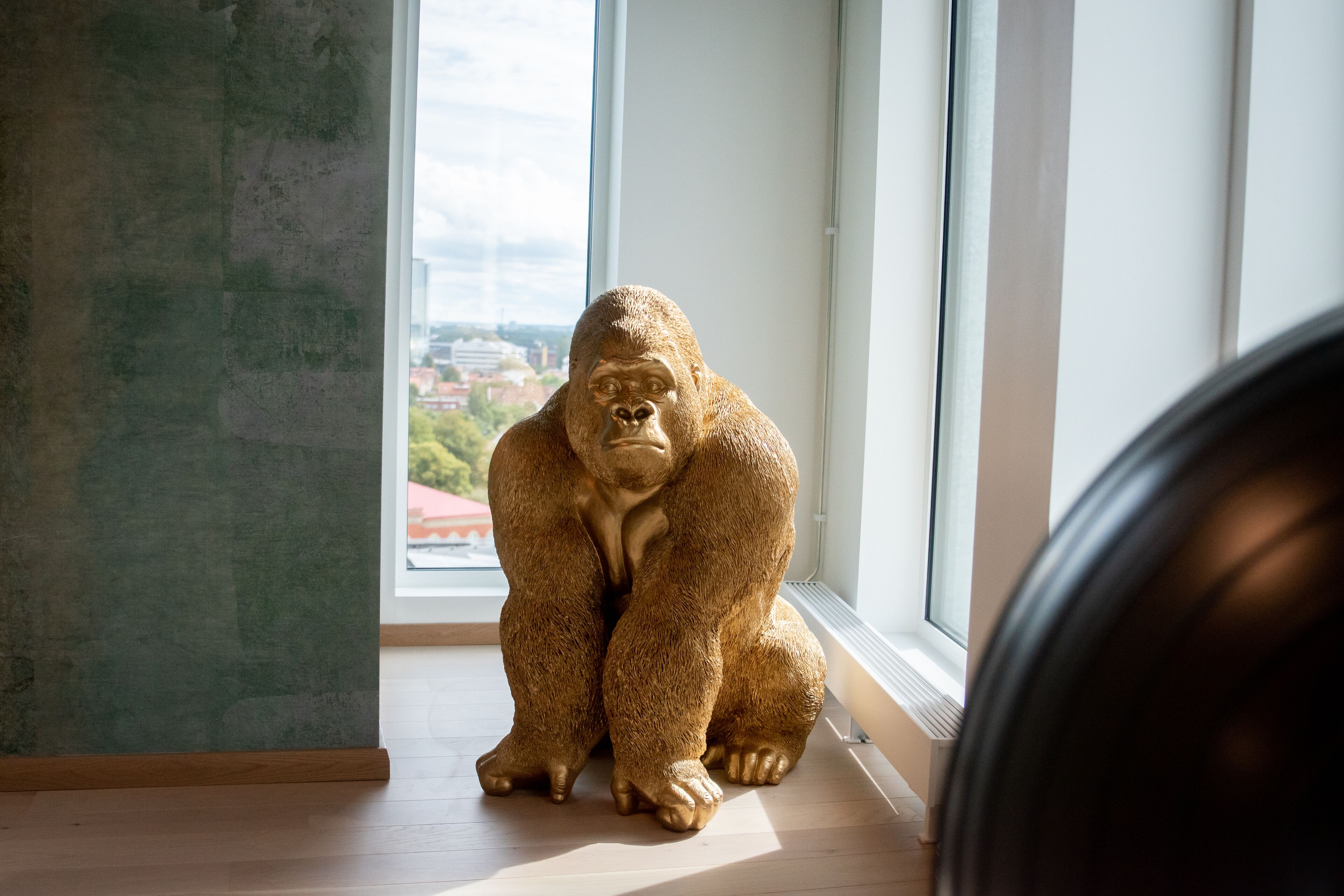 Una estatua de gorila en una habitación con un ventanal grande, suelo de madera y una pared de concreto.