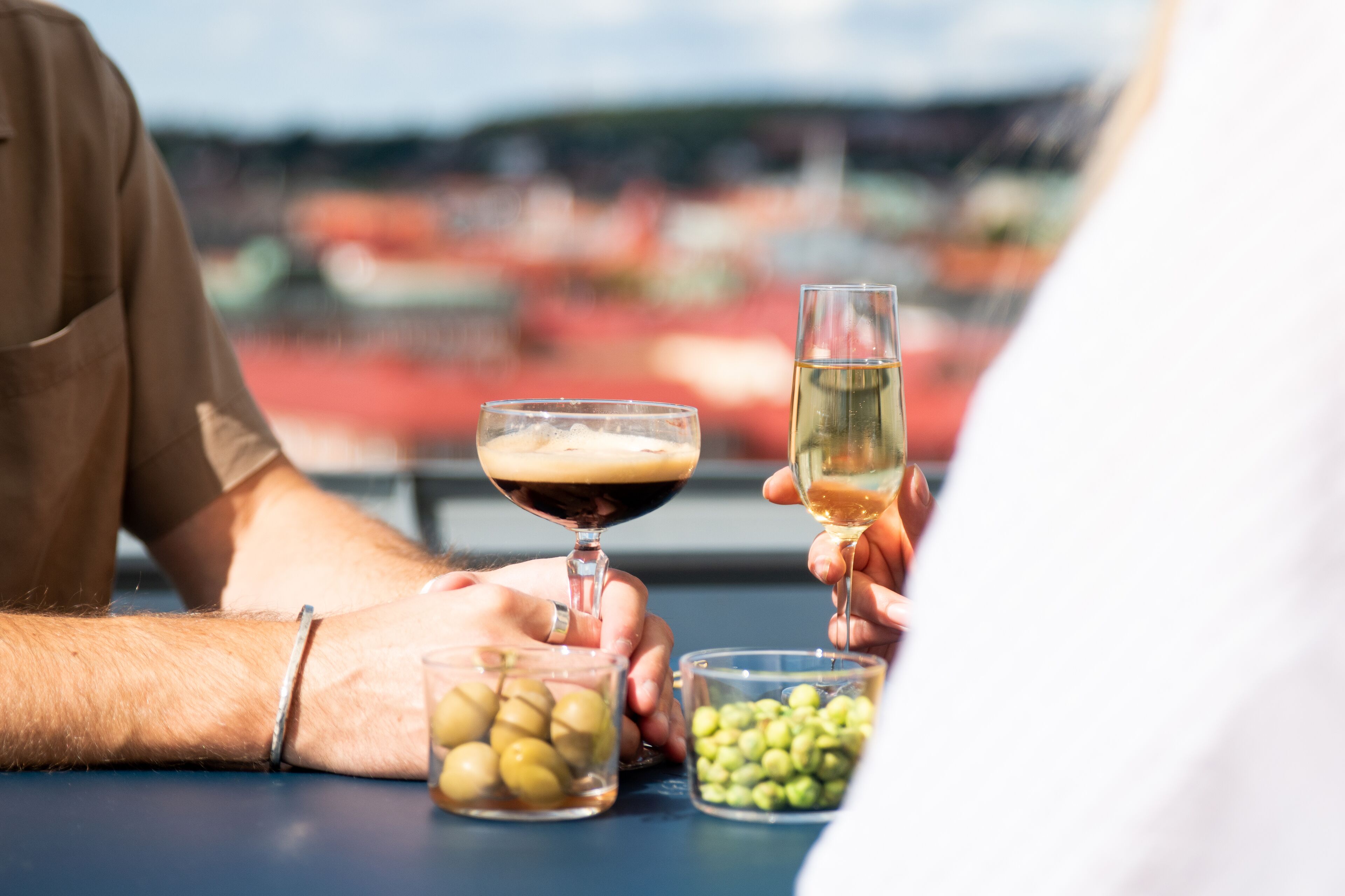 Two people sitting at a table with drinks and olives, overlooking a stadium.