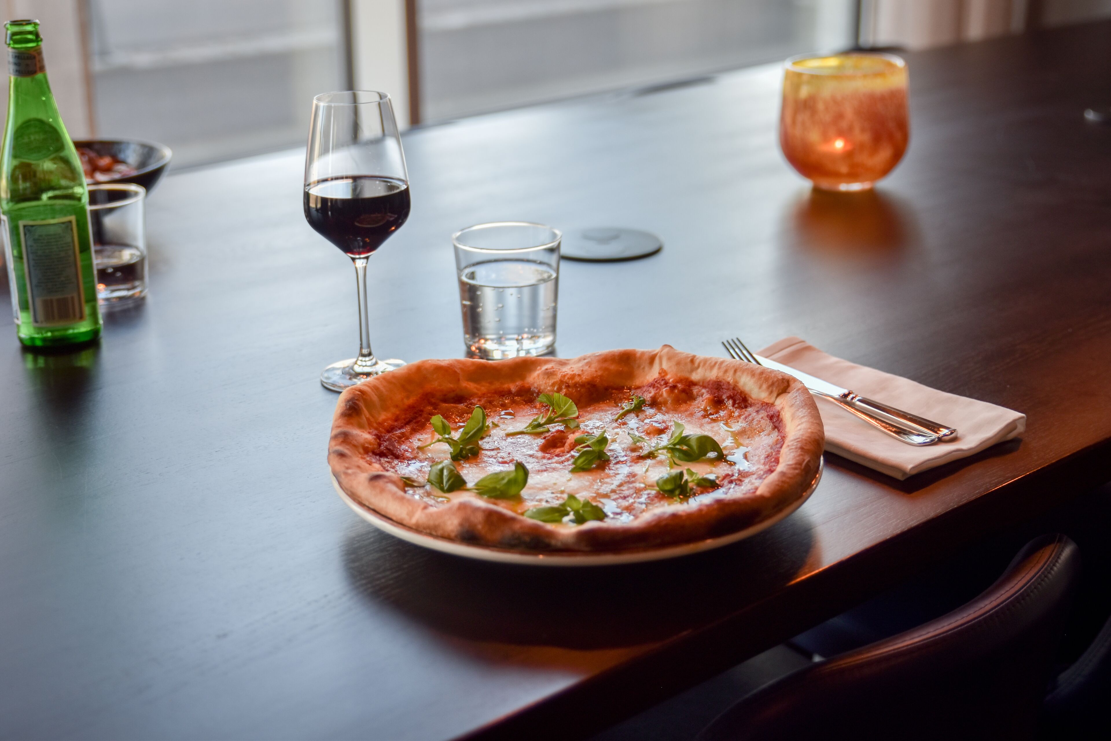 Una pizza sobre una mesa, con una botella de líquido verde, dos vasos de agua y un vaso de líquido rojo.