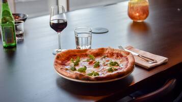 Una pizza sobre una mesa, con una botella de líquido verde, dos vasos de agua y un vaso de líquido rojo.