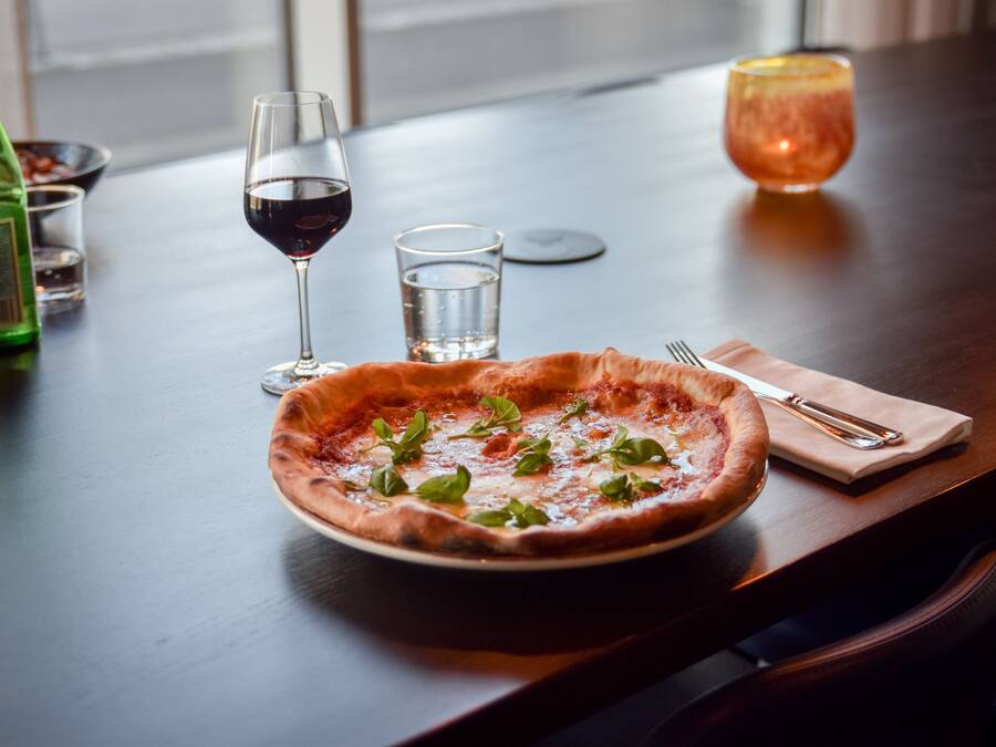 Una pizza sobre una mesa, con una botella de líquido verde, dos vasos de agua y un vaso de líquido rojo.