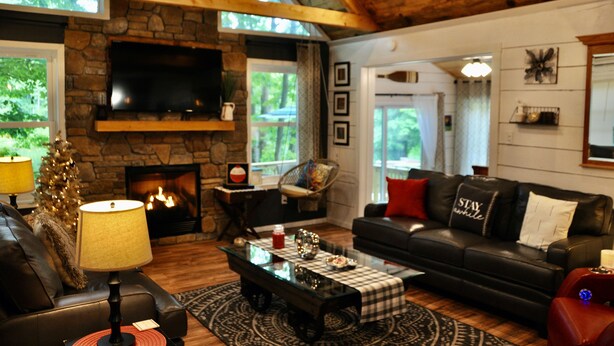 A cozy living room with a stone fireplace, a black leather sofa, a glass coffee table, and a Christmas tree. - Relax Refresh & Reconnect  Lakefront on Autumn Lake, 3min to Salmon River (Orwell)