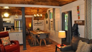 A cozy cabin interior with a wooden ceiling, a dining area with a 'welcome' sign, and a living room with a couch and a lamp. - Relax Refresh & Reconnect  Lakefront on Autumn Lake, 3min to Salmon River (Orwell)