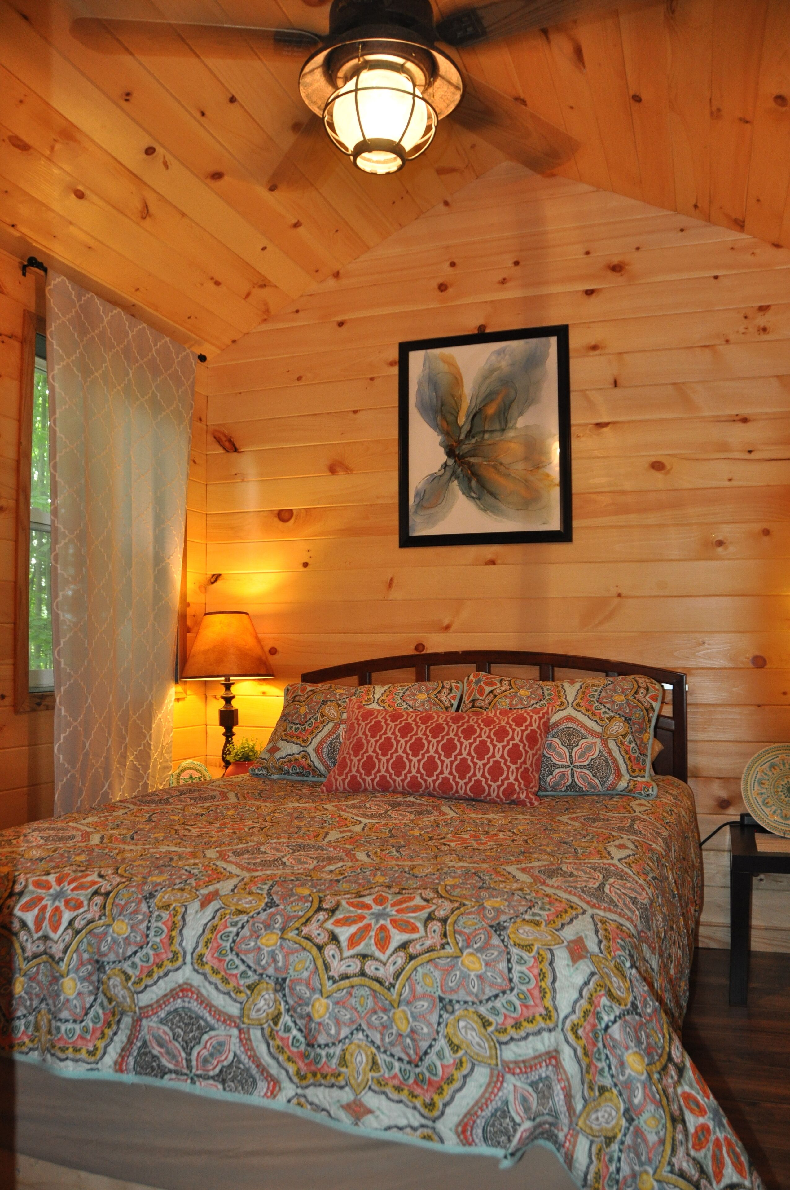 A wooden room with a bed, a lamp, and a ceiling fan.