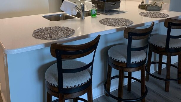 A modern kitchen with white cabinets, a central island with bar stools, a microwave, and a sink. - Catch N Relax Like A Prince  (Mexico Beach)