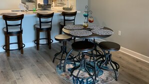 A modern kitchen with white cabinets, a central island with stools, and a dining area with a round table and chairs. - Catch N Relax Like A Prince  (Mexico Beach)