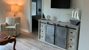 A living room with a patterned armchair, a wooden coffee table, a TV mounted on the wall, and a cabinet with drawers. - Catch N Relax Like A Prince  (Mexico Beach)