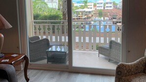 A room with a sliding glass door leading to a balcony with a view of a pool and buildings. - Catch N Relax Like A Prince  (Mexico Beach)