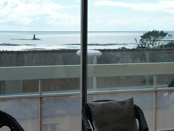 A balcony with a view of the sea, a lighthouse, and a distant island.