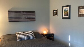 Een slaapkamer met een groot bed, een nachtkastje met een lamp, en drie ingekaderde foto’s aan de muur.