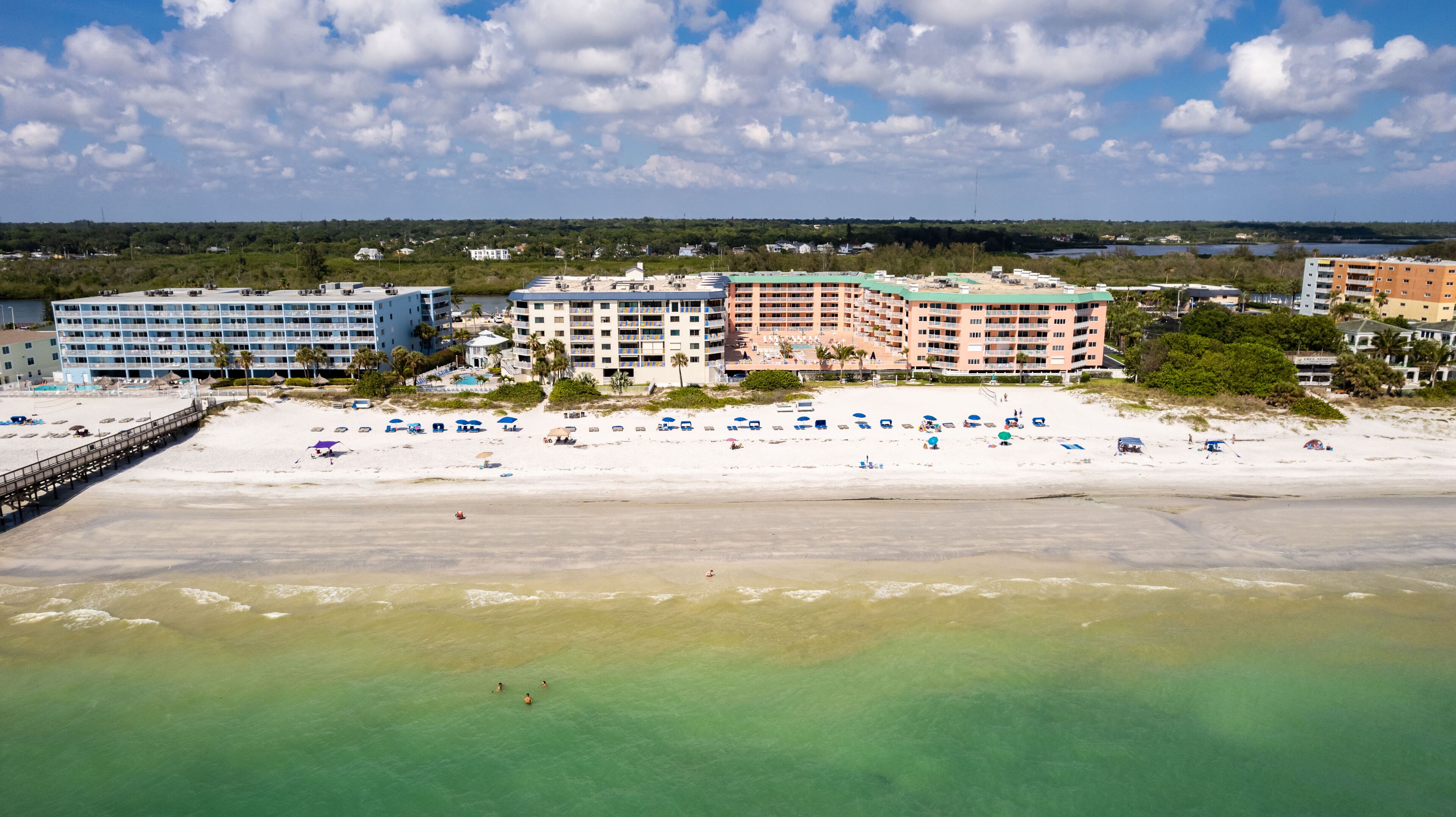 A beachfront hotel with multiple buildings, a sandy beach, and a clear view of the ocean.
