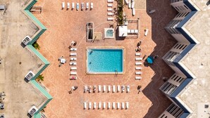 An aerial view of a resort with a central swimming pool surrounded by sun loungers and a few people. - Condominium on beach (Indian Shores)