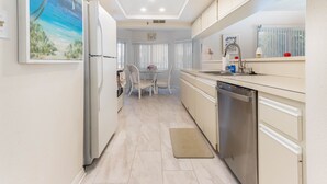 A modern kitchen with a dining area, white cabinetry, and a central island. - Condominium on beach (Indian Shores)
