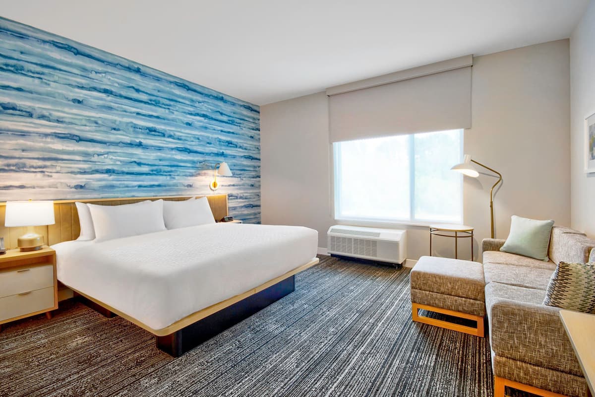 Ein Hotelzimmer mit einem großen Bett, einer Couch, einem Nachttisch, einer Lampe und einem Fenster mit Aussicht.