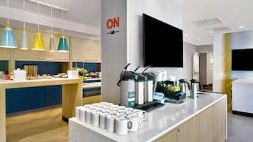 A modern hotel lobby with a coffee station, a flat-screen TV, and a sign indicating the room service area.