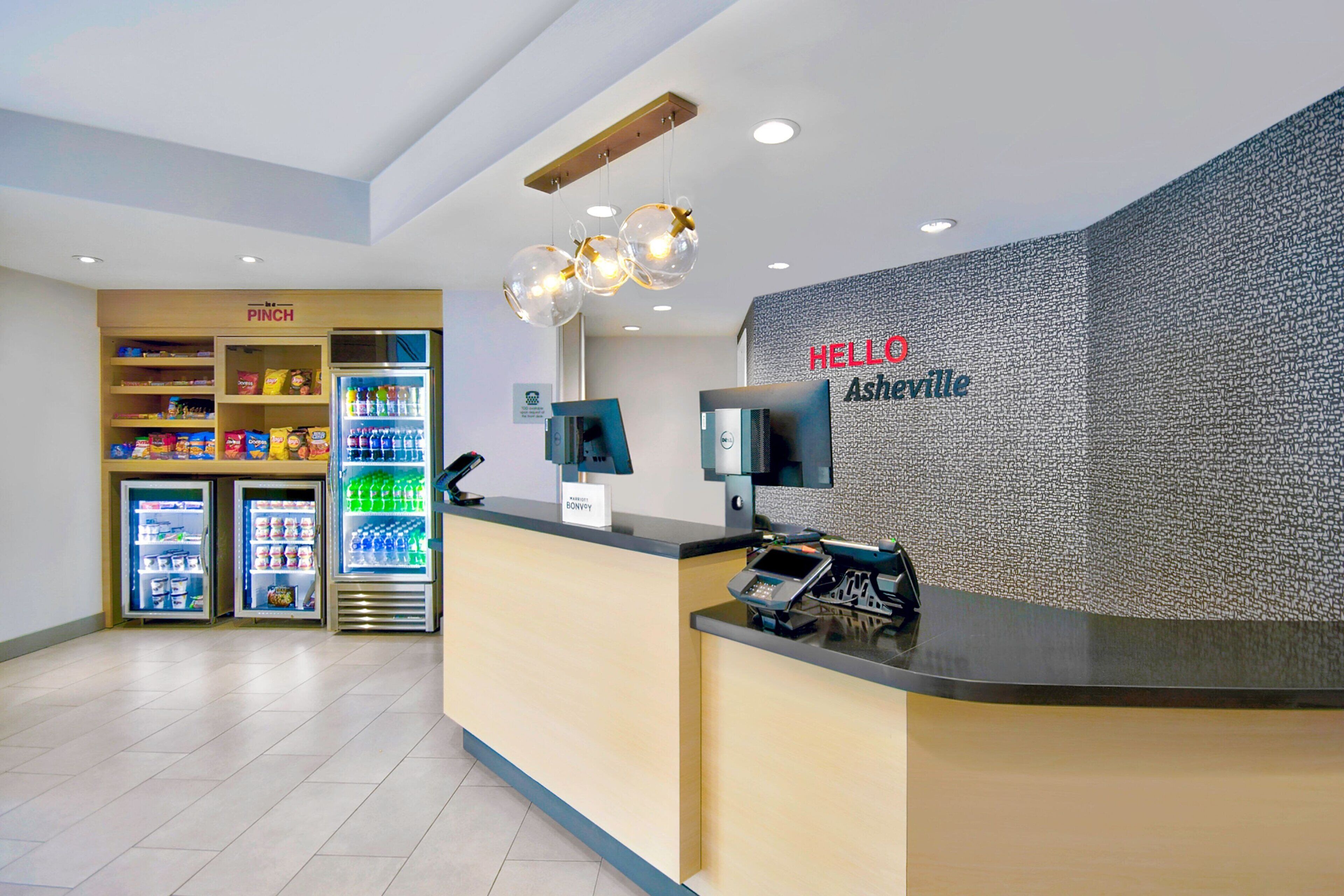 A reception area with a counter, a 'HELLO Asheville' sign, a refrigerator with drinks, and a 'PINCH' sign above it.
