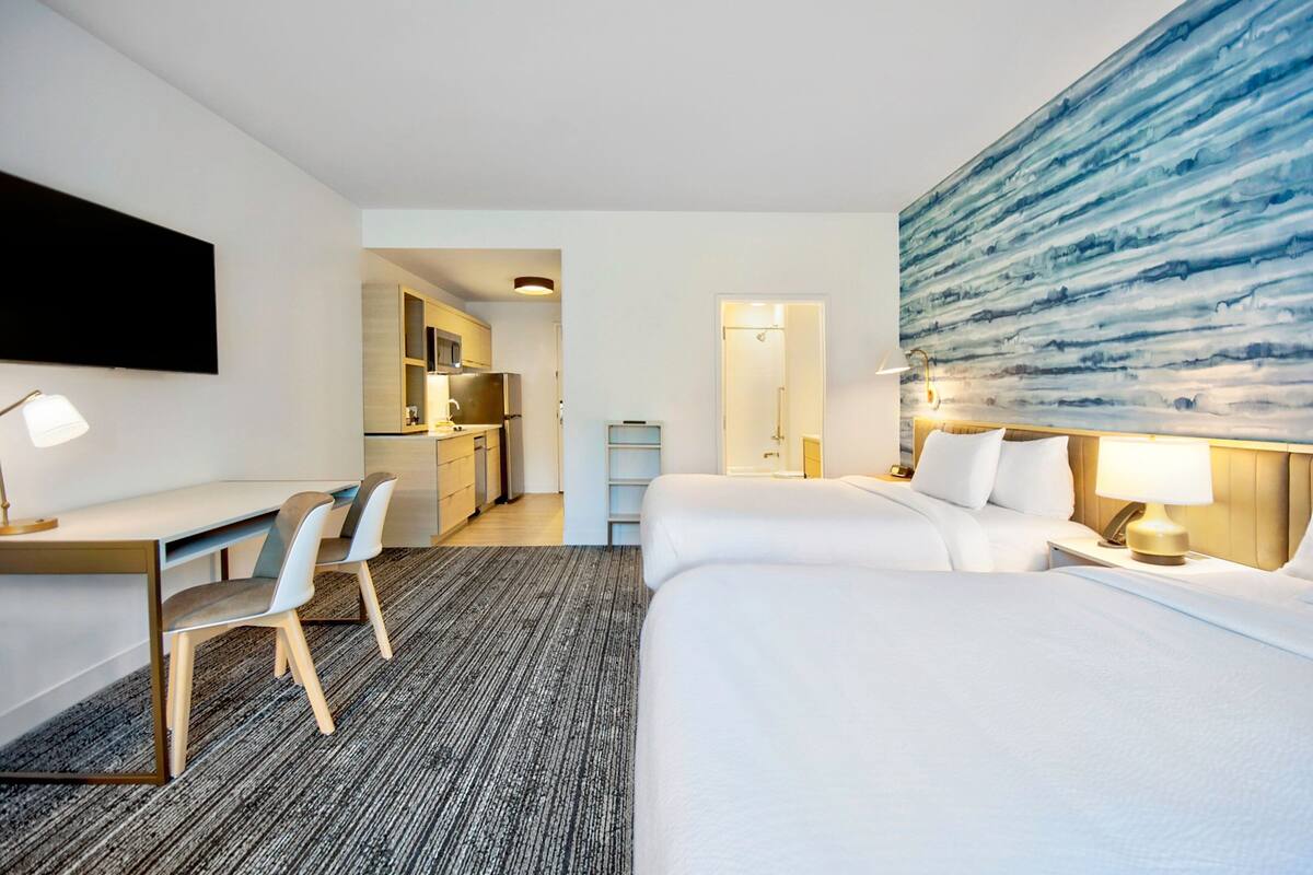 Ein Hotelzimmer mit Bett, Schreibtisch, Stühlen und einer Küchenzeile im Hintergrund.